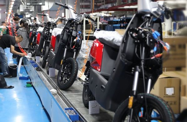 Linha de montagem de veículos elétricos de duas rodas, com trabalhadores montando as motos e bicicletas