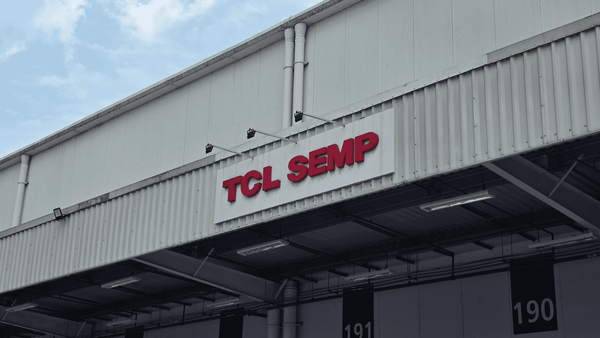 Fachada de um prédio industrial com o letreiro vermelho "TCL SEMP" em destaque, sob um céu nublado