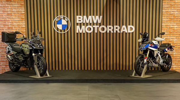 Duas motocicletas BMW Motorrad, uma preta e uma branca com detalhes azuis e vermelhos, em exposição com o logo da marca ao fundo