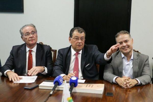 Três homens sentados em uma mesa de reunião, com microfones à frente.