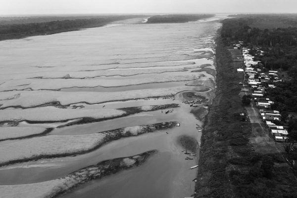 Vista aérea do leito seco do rio Solimões, com bancos de areia expostos e pequenas embarcações, ao lado de uma comunidade