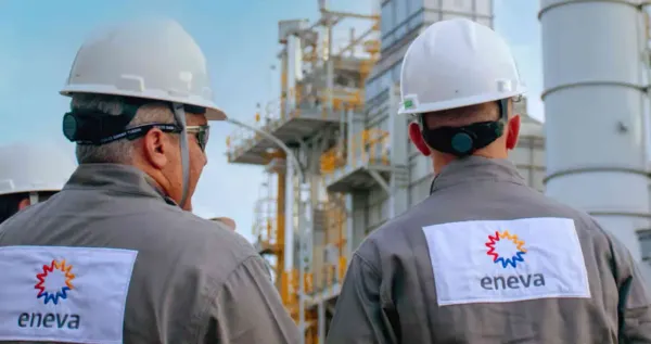 Dois trabalhadores da Eneva, de costas, usando capacetes e uniformes com o logo da empresa, em frente a uma estrutura industrial.