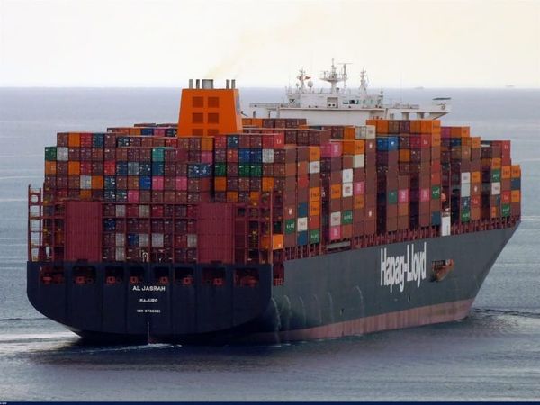 Contêineres empilhados em terminal portuário, com um navio cargueiro ao fundo