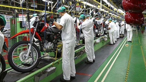 Trabalhadores com uniformes brancos e bonés verdes montam motocicletas vermelhas em linha de produção da Honda em Manaus.