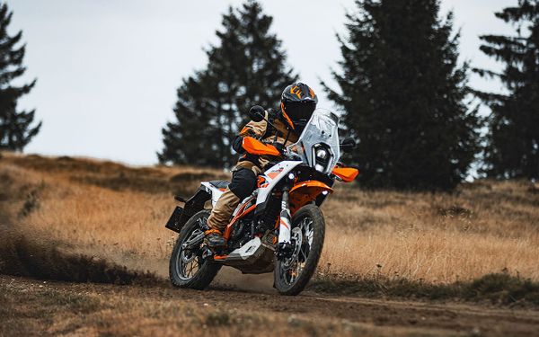Motocicleta KTM 390 Adventure X de cor laranja e preta em destaque, com um fundo desfocado