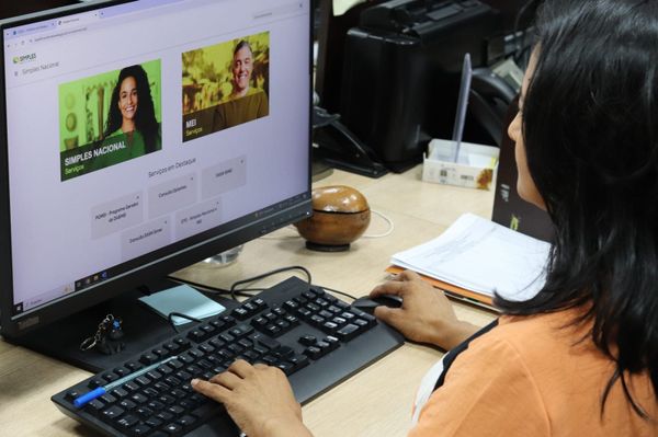 Mulher de costas operando computador que exibe o portal do Simples Nacional em um escritório da Semef em Manaus.