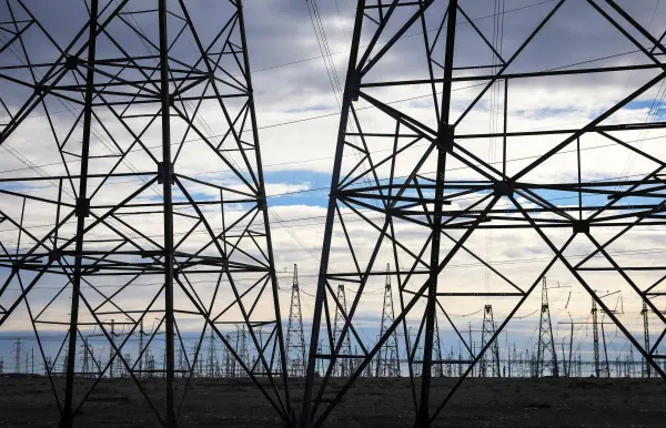 Silhueta de torres de transmissão de energia elétrica em campo aberto, com céu nublado ao fundo