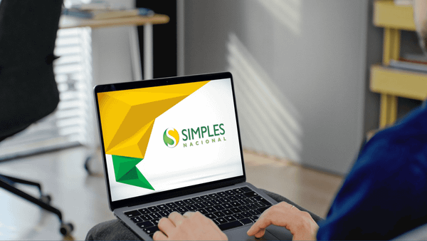 Pessoa sentada usando um notebook com o logo do Simples Nacional na tela, em um ambiente de escritório