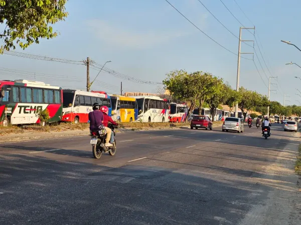 Ônibus de transporte especial parados na lateral de uma via, com carros e motocicletas em movimento na pista, em Manaus