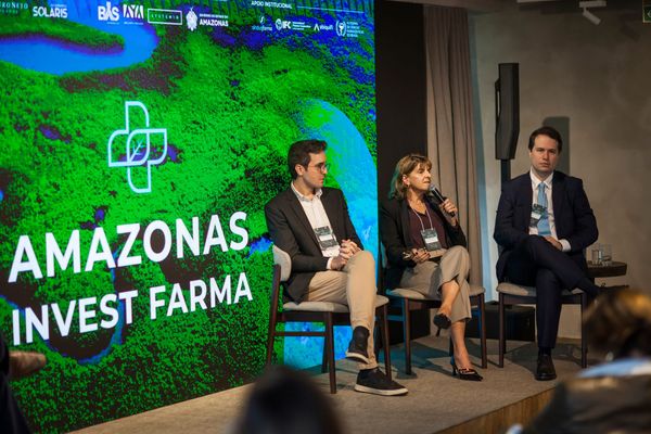 Isabel Reis fala em microfone sentada em painel ao lado de dois homens durante o evento Amazonas Invest Farma em São Paulo.
