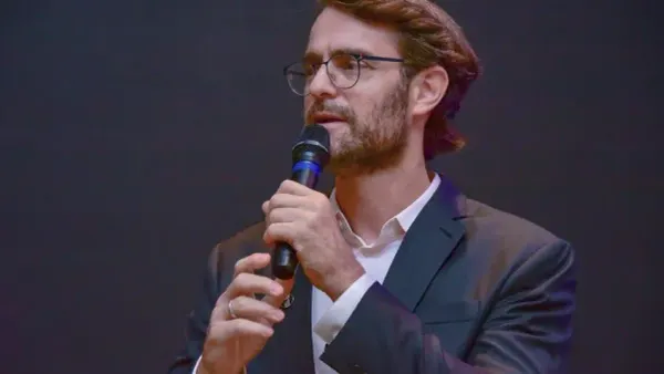 Alexandre Ostrowiecki, de óculos e paletó escuro, fala ao microfone durante evento em setembro de 2026.