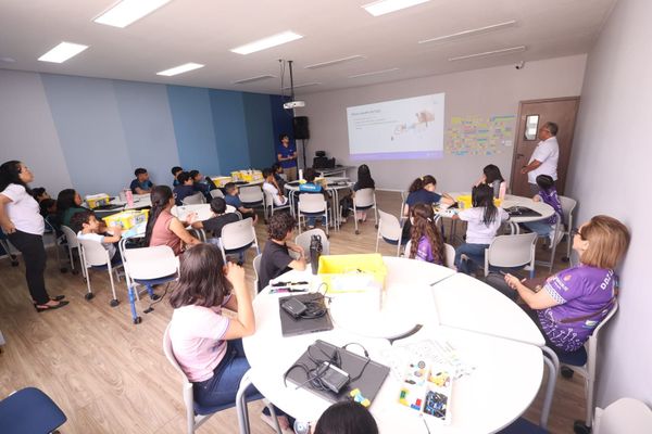 Estudantes sentados em mesas redondas assistem a uma apresentação em sala de aula durante formação em robótica no INDT.