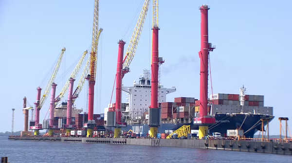 Navio porta-contêineres da Aliança atracado em terminal portuário com grandes guindastes vermelhos e amarelos operando.