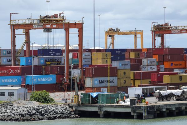 Pátio de terminal portuário com empilhamento de contêineres coloridos de diversas empresas logísticas e guindastes ao fundo.