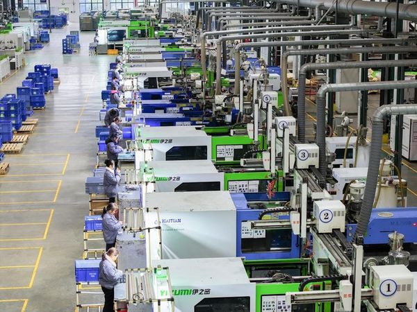 Linha de produção industrial com máquinas automatizadas e operários em uniformes cinza operando equipamentos numerados.