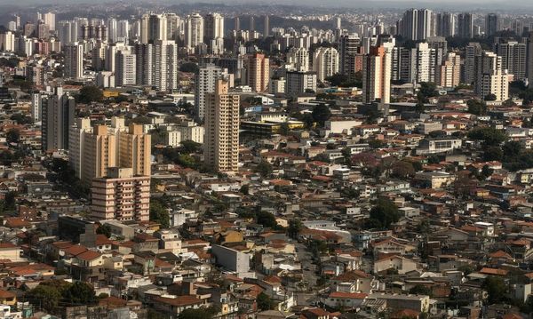 Vista aérea de uma área urbana com densidade de casas e prédios residenciais ao fundo sob luz solar.