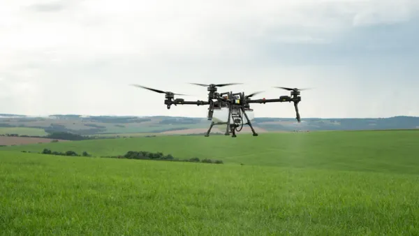 Drone agrícola de grande porte sobrevoa plantação verde sob céu nublado.