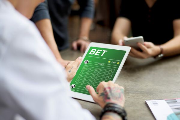 Pessoa segura tablet exibindo interface de site de apostas esportivas com a palavra BET em destaque.