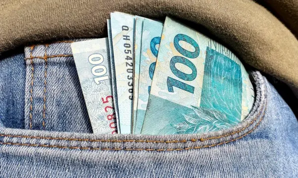 Cédulas de cem reais dobradas dentro do bolso de uma calça jeans azul.