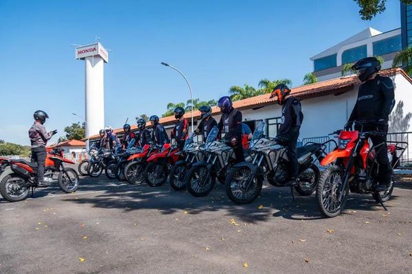 Motociclistas em treinamento de pilotagem segura no Centro Educacional de Trânsito Honda, com torre da marca ao fundo.