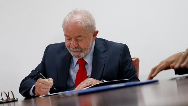 O presidente Luiz Inácio Lula da Silva assina documento oficial sobre uma mesa de madeira.