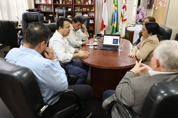 Pessoas reunidas em volta de uma mesa de madeira com um notebook aberto durante reunião no Ministério Público do Amazonas.
