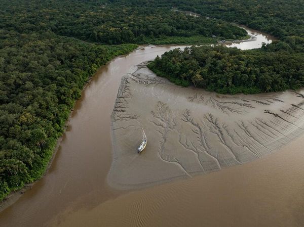 Vista aérea de um barco navegando em rio sinuoso cercado por floresta densa e bancos de areia na região amazônica.