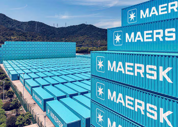 Pátio repleto de contêineres azuis com o logotipo da Maersk empilhados sob céu azul.
