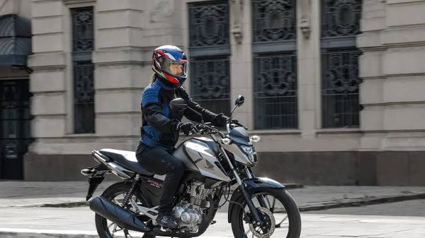 Pessoa pilotando uma motocicleta Honda prateada em uma via urbana em frente a um prédio histórico.