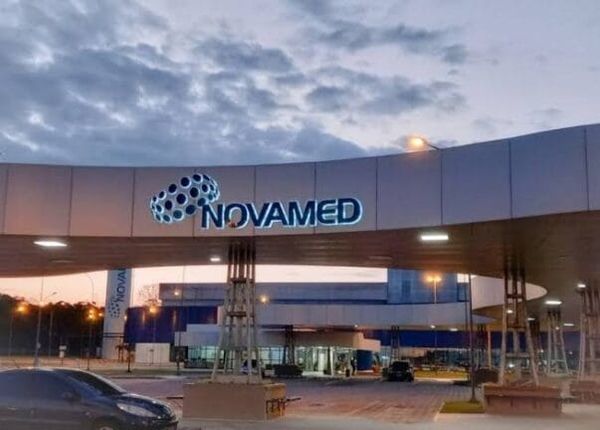 Fachada da fábrica da Novamed em Manaus com letreiro iluminado sob estrutura curva de concreto ao entardecer.