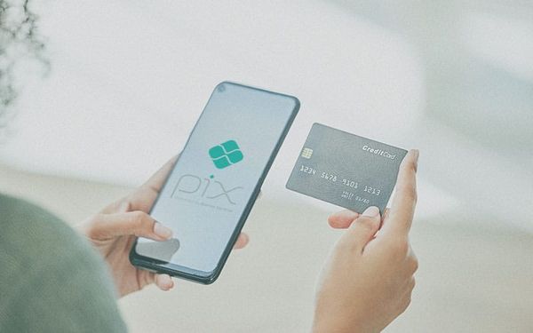 Mãos seguram um smartphone com o logotipo do Pix na tela e um cartão de crédito físico.