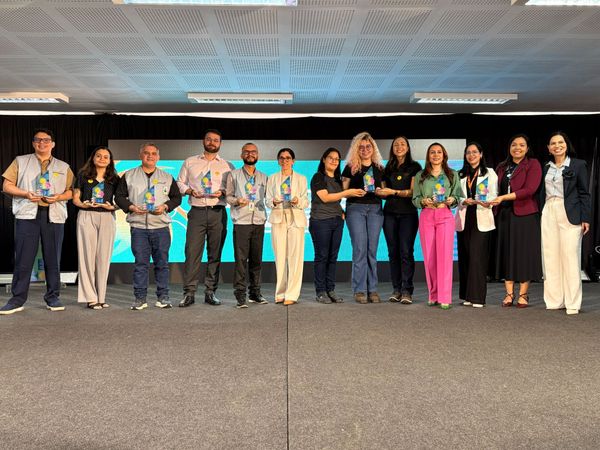 Grupo de premiados segurando troféus transparentes no palco durante a entrega do Prêmio IEL 2026 em Manaus.