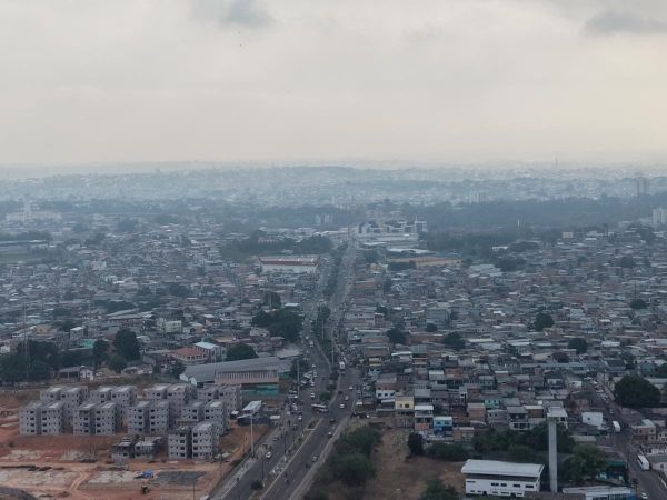 Vista aérea de Manaus coberta por fumaça cinzenta, com prédios e casas sob céu nublado em 17 de setembro de 2026.