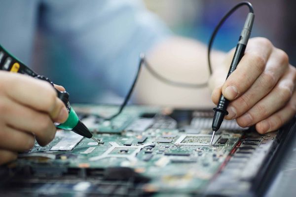 Mãos de um técnico utilizando ferramentas de precisão para realizar reparos em uma placa de circuito eletrônico.