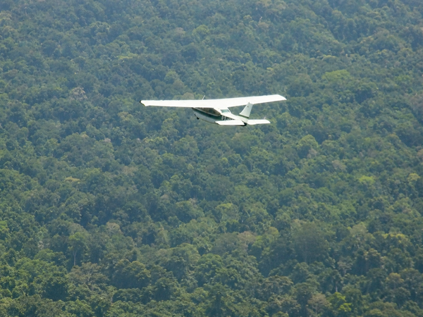 Avião de pequeno porte sobrevoa área de floresta densa na região amazônica.