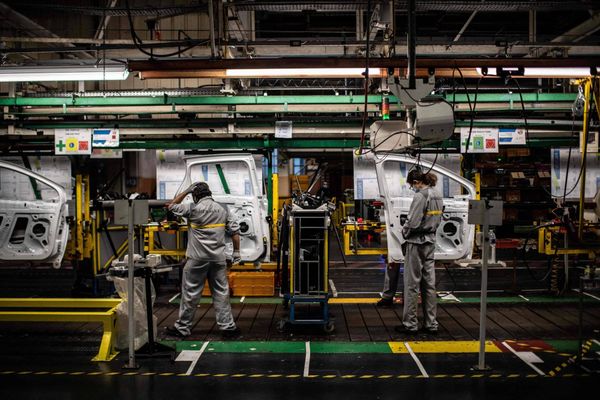 Trabalhadores em linha de montagem industrial manuseiam estruturas de portas de veículos em fábrica da Renault.