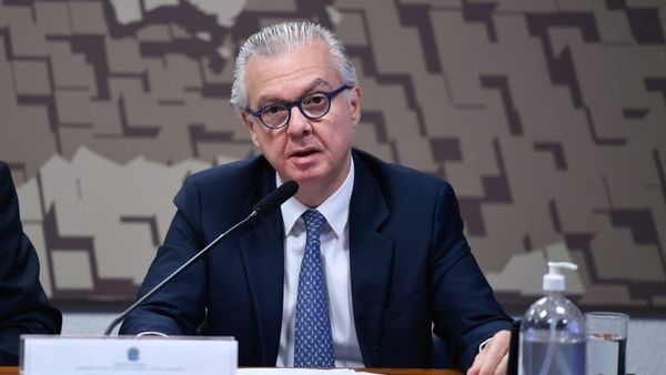O embaixador Rodrigo de Azeredo Santos, de óculos e terno azul, fala ao microfone durante uma mesa de reunião.