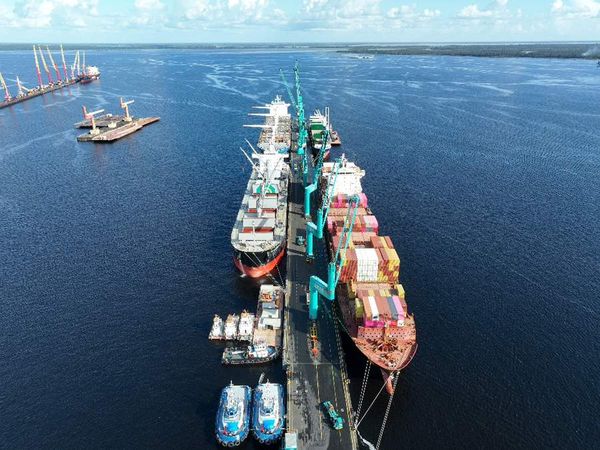 Vista aérea de navios cargueiros atracados no terminal portuário do Super Terminais em Manaus, com guindastes verdes.