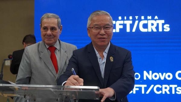 Gilberto Takao Sakamoto, presidente do CFT, assina documento em púlpito transparente diante de painel azul do Sistema CFT/CRTs.