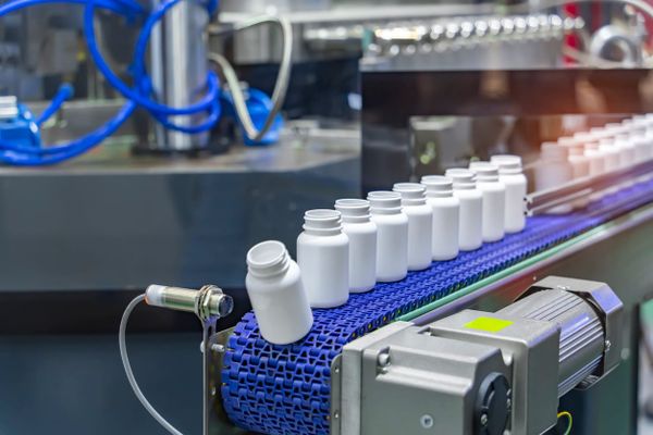 Frascos brancos de suplementos em linha de produção automatizada com esteira azul em uma fábrica.