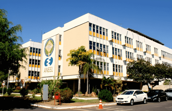 Fachada do edifício da sede da Aneel, em Brasília, com logotipo da agência e carros estacionados à frente.