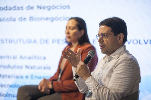 Carlos Henrique Carvalho fala ao microfone no palco, com Andréia Freitas Vieira ao fundo e slide da estrutura do CBA