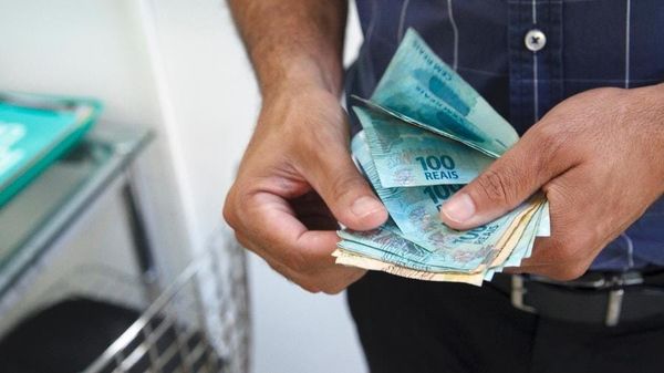 Mãos de um homem contando diversas cédulas de cem reais.