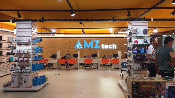 Interior da loja AMZ Tech em Manaus com balcão de atendimento, cadeiras laranjas e prateleiras com produtos de tecnologia.