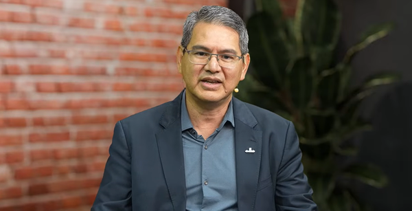 Marcos Bento, presidente da Abraciclo, veste paletó azul e óculos, falando em frente a uma parede de tijolos e uma planta.