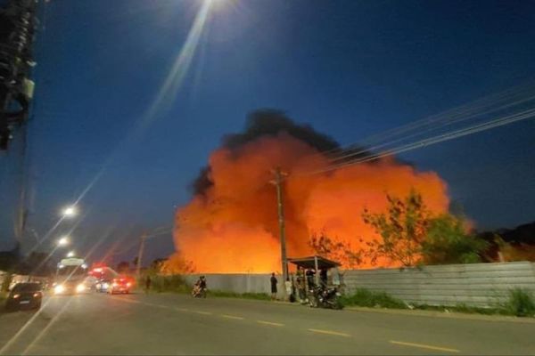 Chamas e fumaça alaranjada saindo de terreno atrás de muro no Distrito Industrial II, em Manaus, durante a noite.