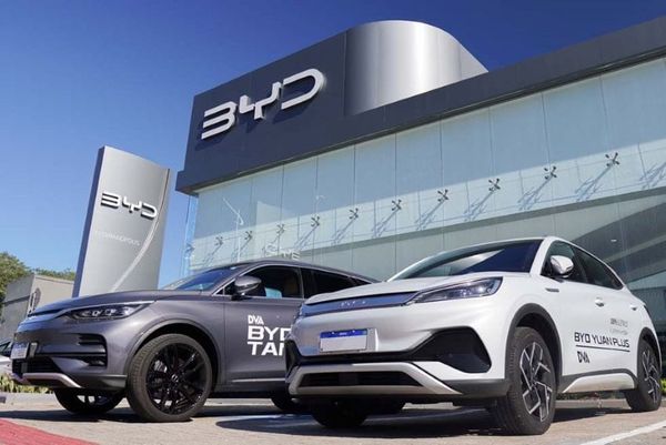 Dois veículos da BYD, um cinza e um branco modelo Yuan Plus, estacionados em frente a uma concessionária da marca.