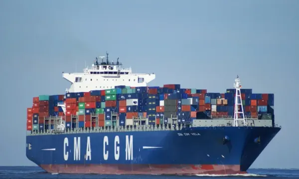 Navio porta-contêineres azul da armadora CMA CGM carregado com diversas unidades coloridas navegando em mar aberto.
