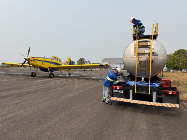 Funcionários da Águas de Manaus operam caminhão-pipa para abastecer avião amarelo Air Tractor em pista de pouso.
