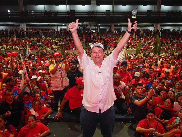 Eduardo Braga de braços erguidos e segurando um microfone diante de uma multidão de apoiadores vestidos de vermelho.